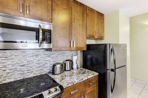 A kitchen with wooden cabinets, a stainless steel microwave, a black refrigerator, a gas stove, and a tiled backsplash. - Maui Paradise Awaits! Direct Ocean Views, Swimmable Beach & On-Site Dining (Lahaina)
