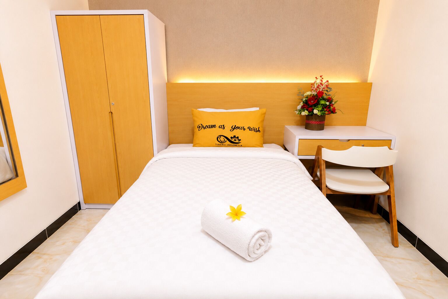 A hotel room with a bed, a desk, a chair, a wardrobe, and a decorative flower arrangement.