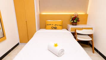 Habitación de hotel con cama, escritorio, silla, armario y un arreglo floral decorativo.