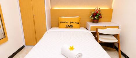 A hotel room with a bed, a desk, a chair, a wardrobe, and a decorative flower arrangement.