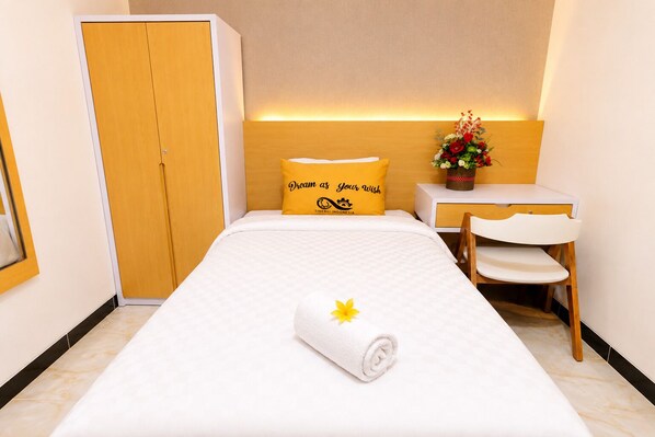A hotel room with a bed, a desk, a chair, a wardrobe, and a decorative flower arrangement.