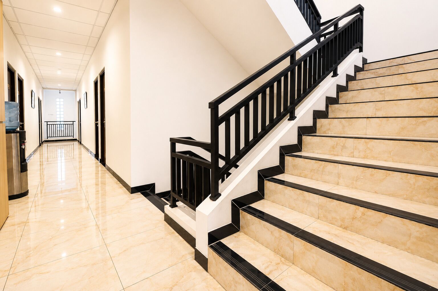A corridor leading to a staircase with a black railing and beige steps.