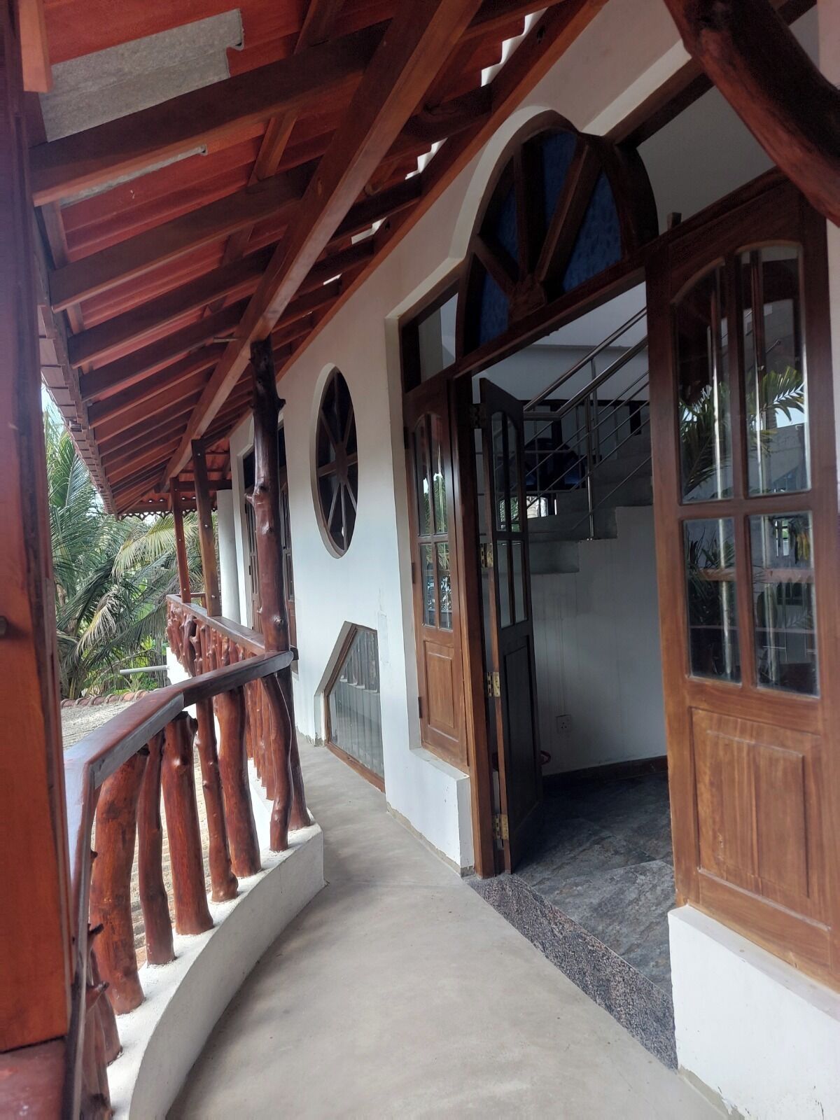Un'area esterna coperta con ringhiera in legno, una panchina curva e vista su un edificio con ampie finestre e un ingresso.
