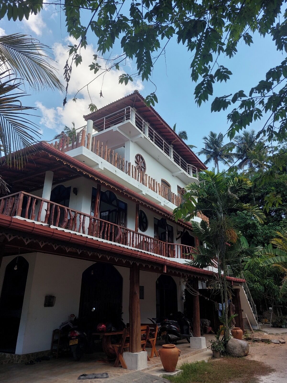 A two-story building with a balcony, surrounded by tropical vegetation.