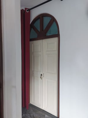 Una puerta blanca con un arco de madera encima, una cortina roja y un suelo de baldosas.