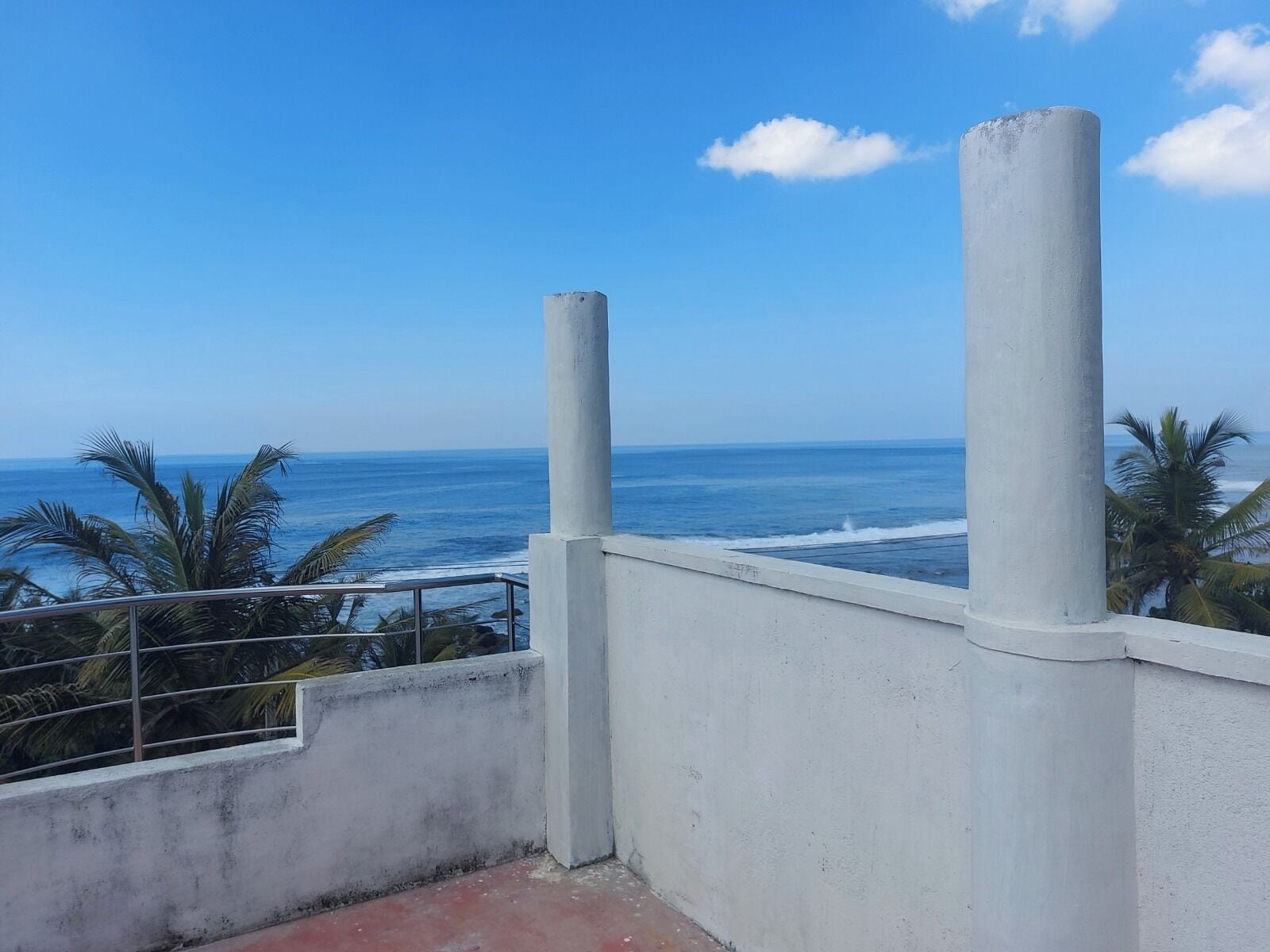 A balcony with a view of the ocean and palm trees.