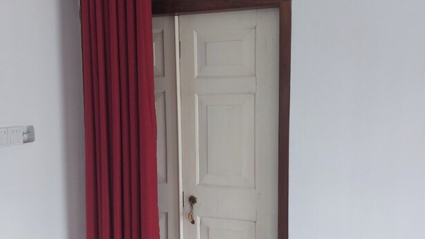 Une porte blanche avec un cadre en bois et un rideau rouge, partiellement tiré sur le côté.