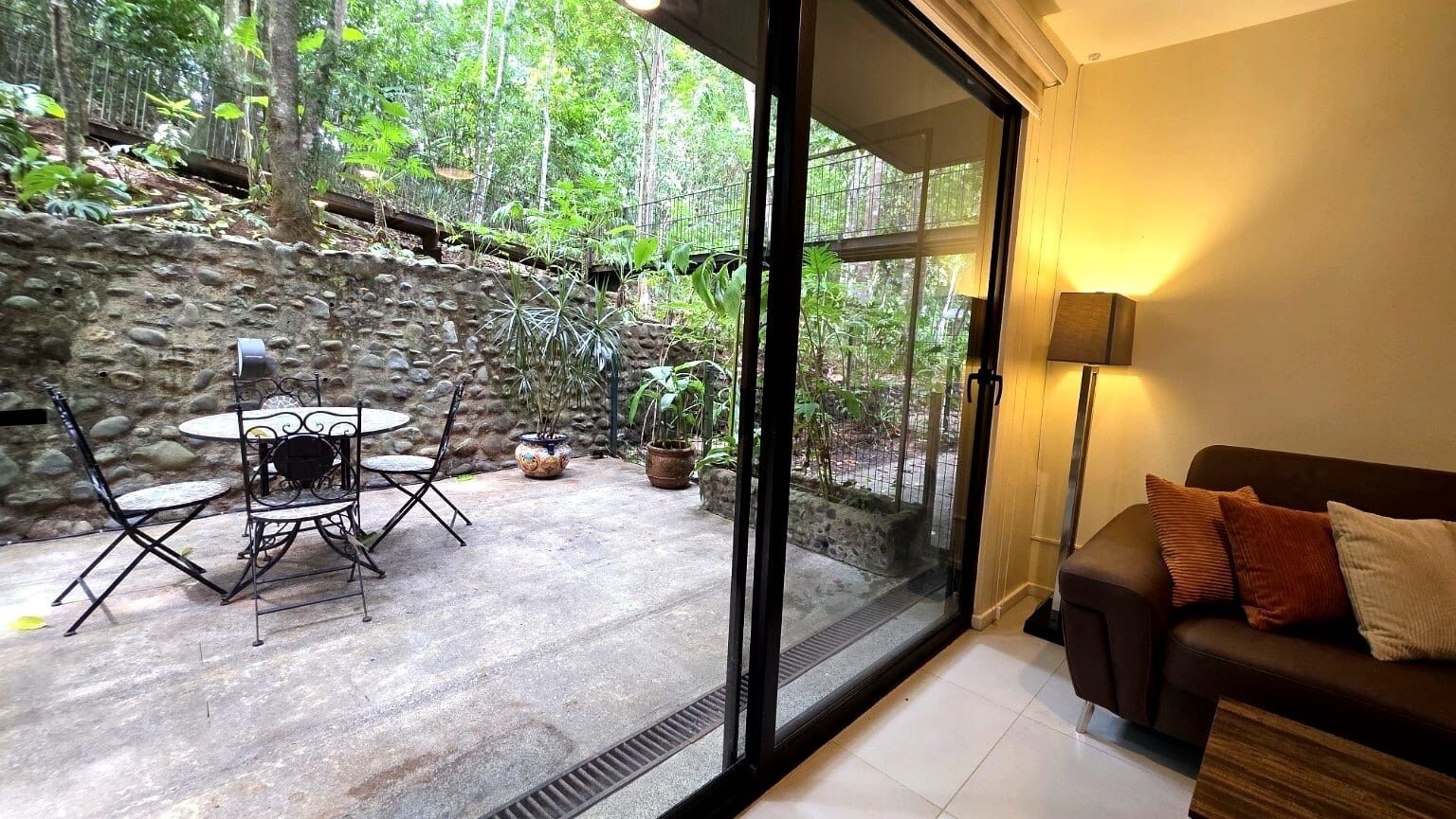 Une pièce dotée d’une porte vitrée donnant sur un mur de pierre et un jardin. À l’intérieur, on trouve un canapé et une table avec des chaises.