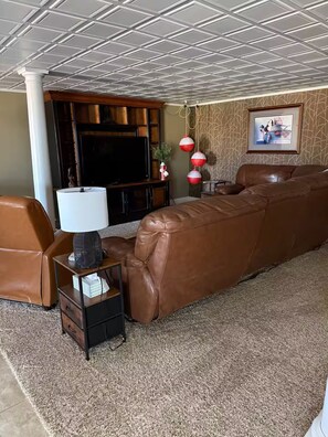 A living room with a brown leather sofa, a flat-screen TV, a coffee table, and a patterned carpet.