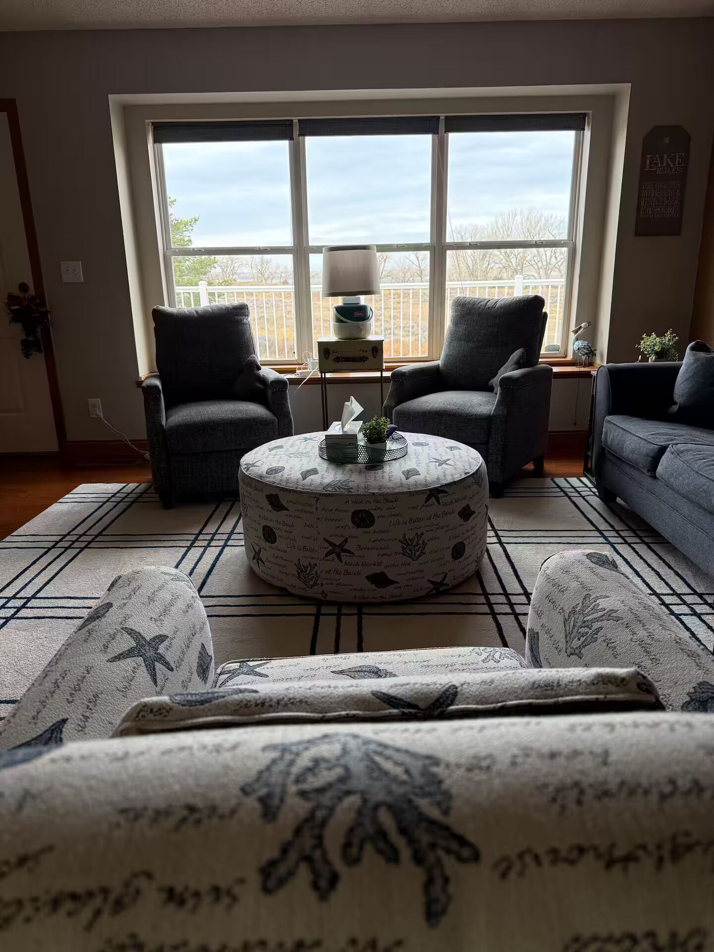 Ein Wohnzimmer mit zwei Sesseln, einem Sofa, einem runden Couchtisch und Blick ins Freie durch große Fenster.