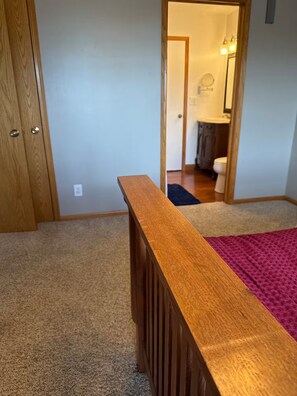 A room with a wooden headboard, carpeted floor, and a visible bathroom in the background. - Spacious 4-bedroom house at peaceful Lake McConaughy. (Brule)