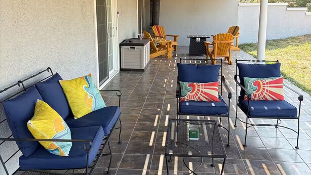 Un'area patio esterna coperta con posti a sedere, tra cui un divano e delle poltrone, e un tavolino.