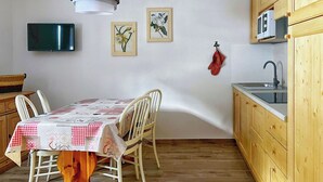Ruokailutila, jossa on neljälle katettu ruokapöytä, puiset tuolit, puulattia, puukehikkoiset keittiökaapit, mikroaaltouuni ja seinälle ripustettu pyyhe.