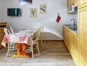 Ein Essbereich mit Tisch für vier Personen, Holzstühle, Holzboden, eine Küche mit Holdschränken, einer Mikrowelle und einem aufgehängten Handtuch.