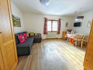 Ein Wohnzimmer mit einer Couch, einem Esstisch mit Stühlen, einem Heizkörper und einem Fenster mit Vorhängen.