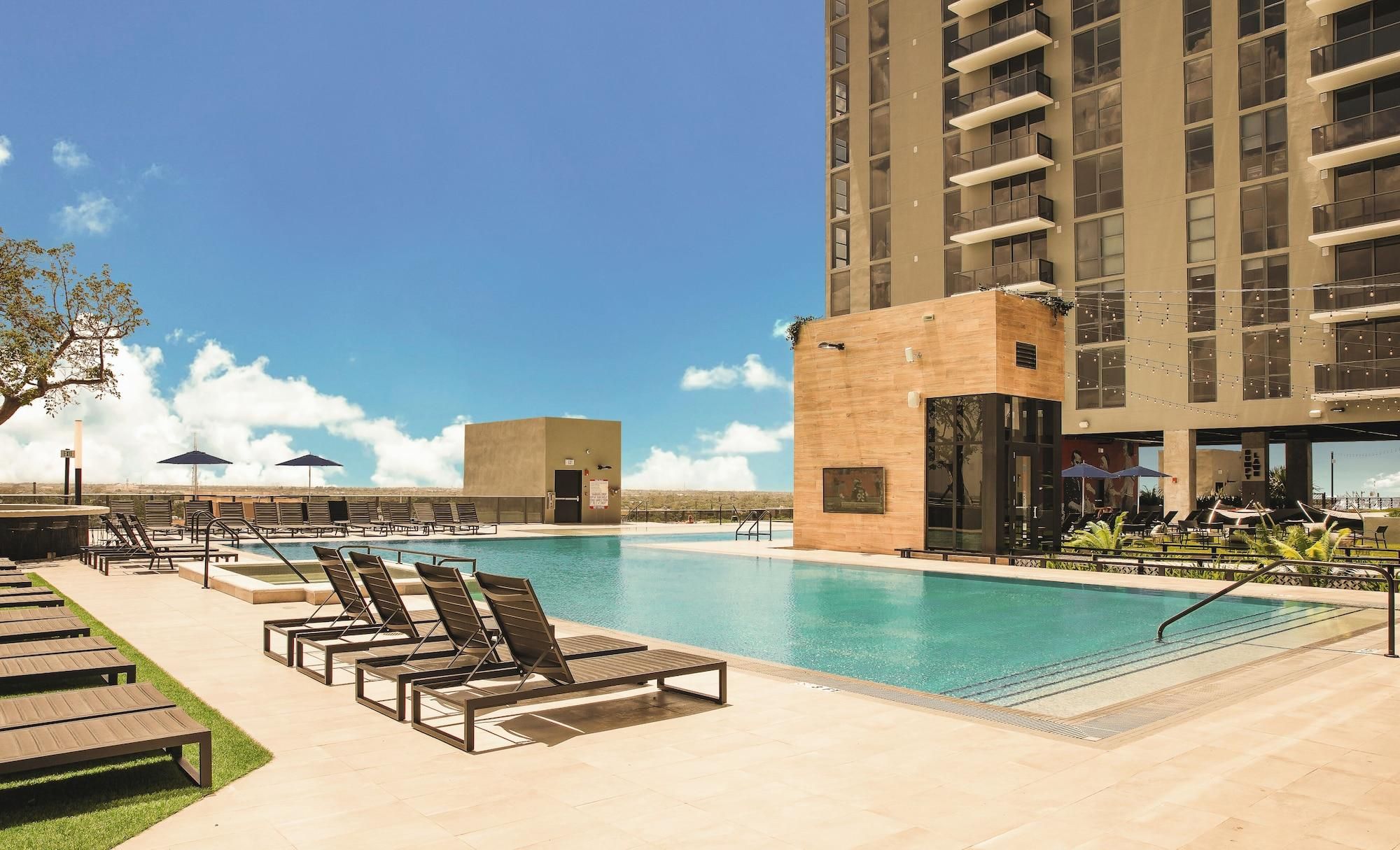 A swimming pool with lounge chairs and a building with balconies.