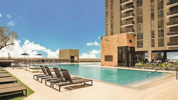 Uma piscina com espreguiçadeiras e um prédio com sacadas.