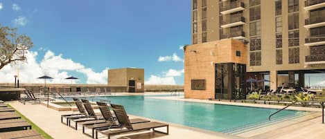 A swimming pool with lounge chairs and a building with balconies.