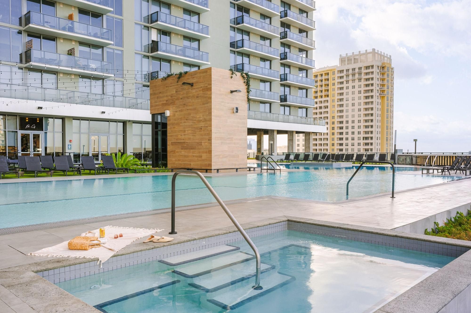 A swimming pool with lounge chairs and a wooden structure, surrounded by modern buildings.