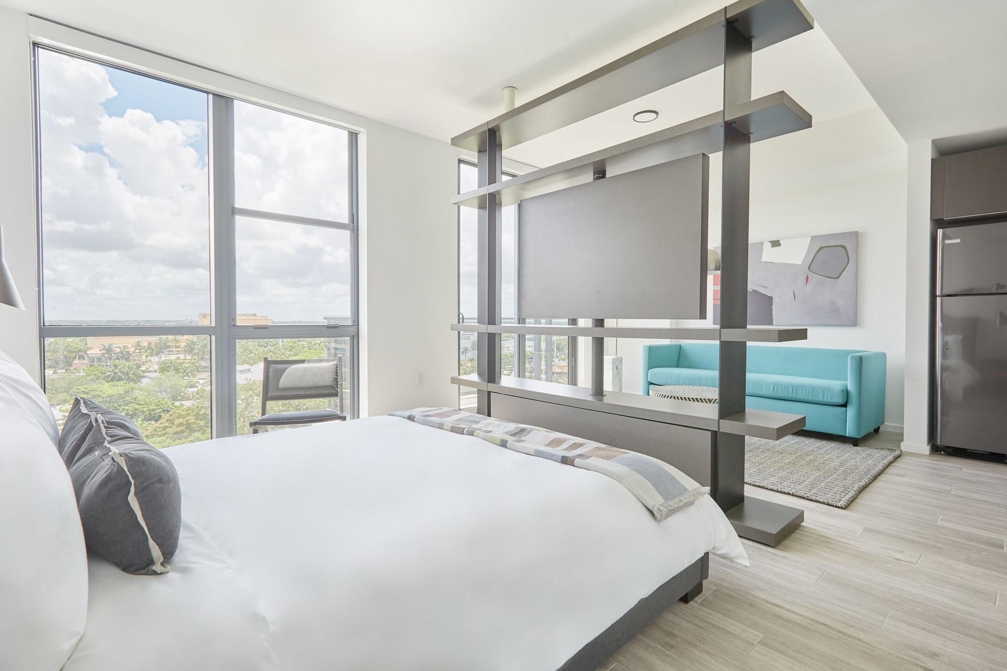 A modern bedroom with a large bed, a sofa, a TV, and a view of the city.