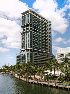 A modern high-rise hotel with multiple balconies, a waterfront view, and a palm-lined promenade. - Sonder at Riverwalk (Fort Lauderdale)