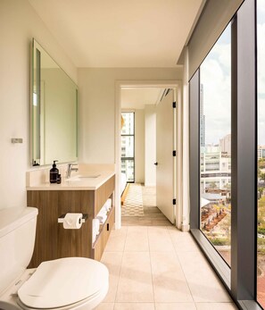 A modern bathroom with a large window, a toilet, a sink, and a mirror. - Sonder at Riverwalk (Fort Lauderdale)