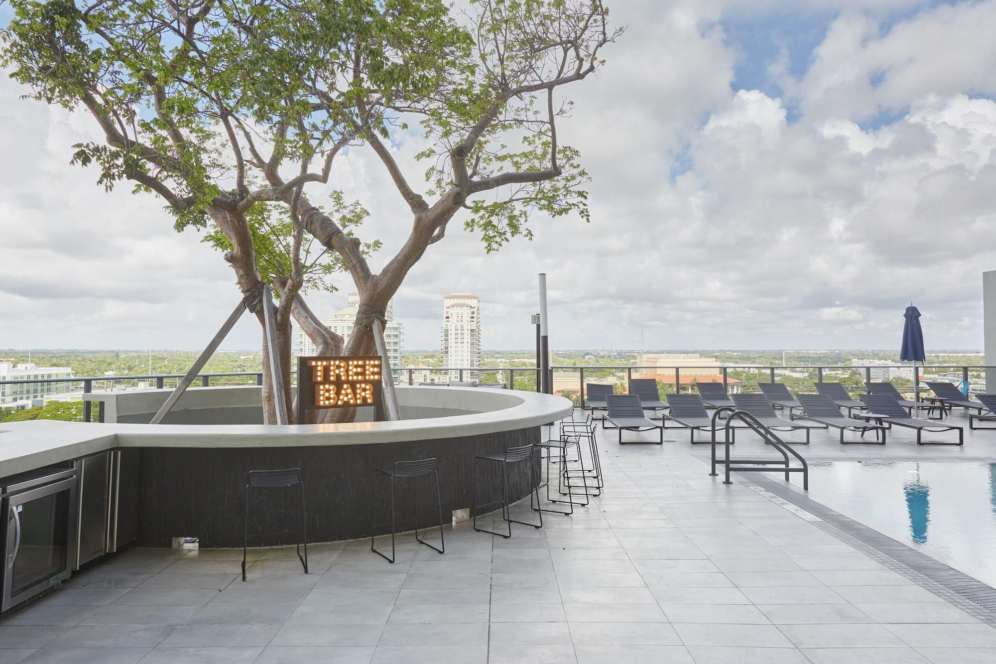 Un bar en la azotea con piscina, sillones de descanso y un cartel con el nombre del bar.