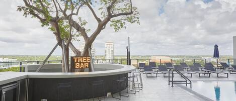 Un bar en la azotea con piscina, sillones de descanso y un cartel con el nombre del bar.