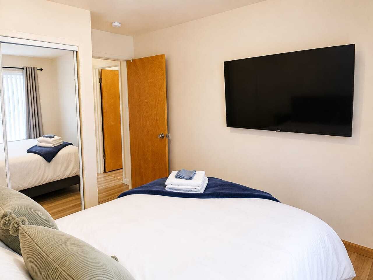 Habitación de hotel con cama, televisión montada en la pared y puerta que da a otra habitación.