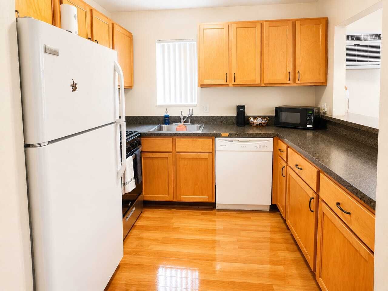 A kitchen with wooden cabinets, a white refrigerator, a dishwasher, a microwave, and a window with blinds.