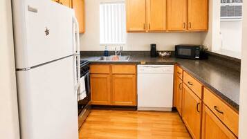 A kitchen with wooden cabinets, a white refrigerator, a dishwasher, a microwave, and a window with blinds.