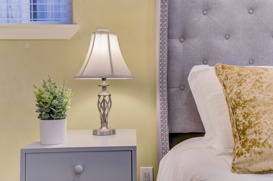 A bedroom with a bed, a bedside table with a lamp, and a potted plant.