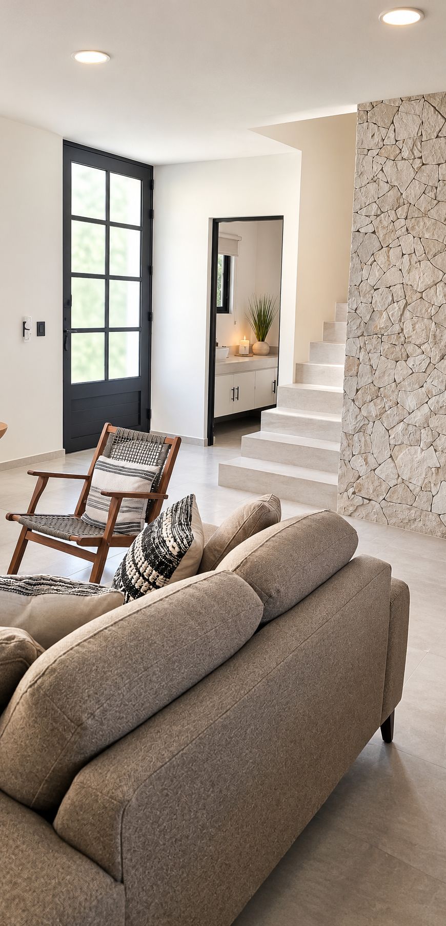A modern living room with a sofa, a wooden chair, and a staircase leading to an upper level.