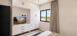 A bedroom with a bed, a TV mounted on the wall, a window with curtains, and a wardrobe. - ​Tranquil Modern Haven Chuburná Beach & Mérida (Merida)