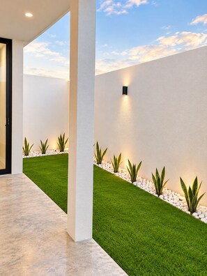 Un bâtiment moderne avec une façade extérieure caractérisée par un toit plat, un sol en béton et une série de jardinières contenant des plantes vertes disposées le long du mur.
