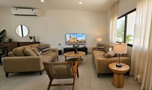 A modern living room with two sofas, a round coffee table, a side table with a lamp, a TV, and a large window with curtains. - ​Tranquil Modern Haven Chuburná Beach & Mérida (Merida)