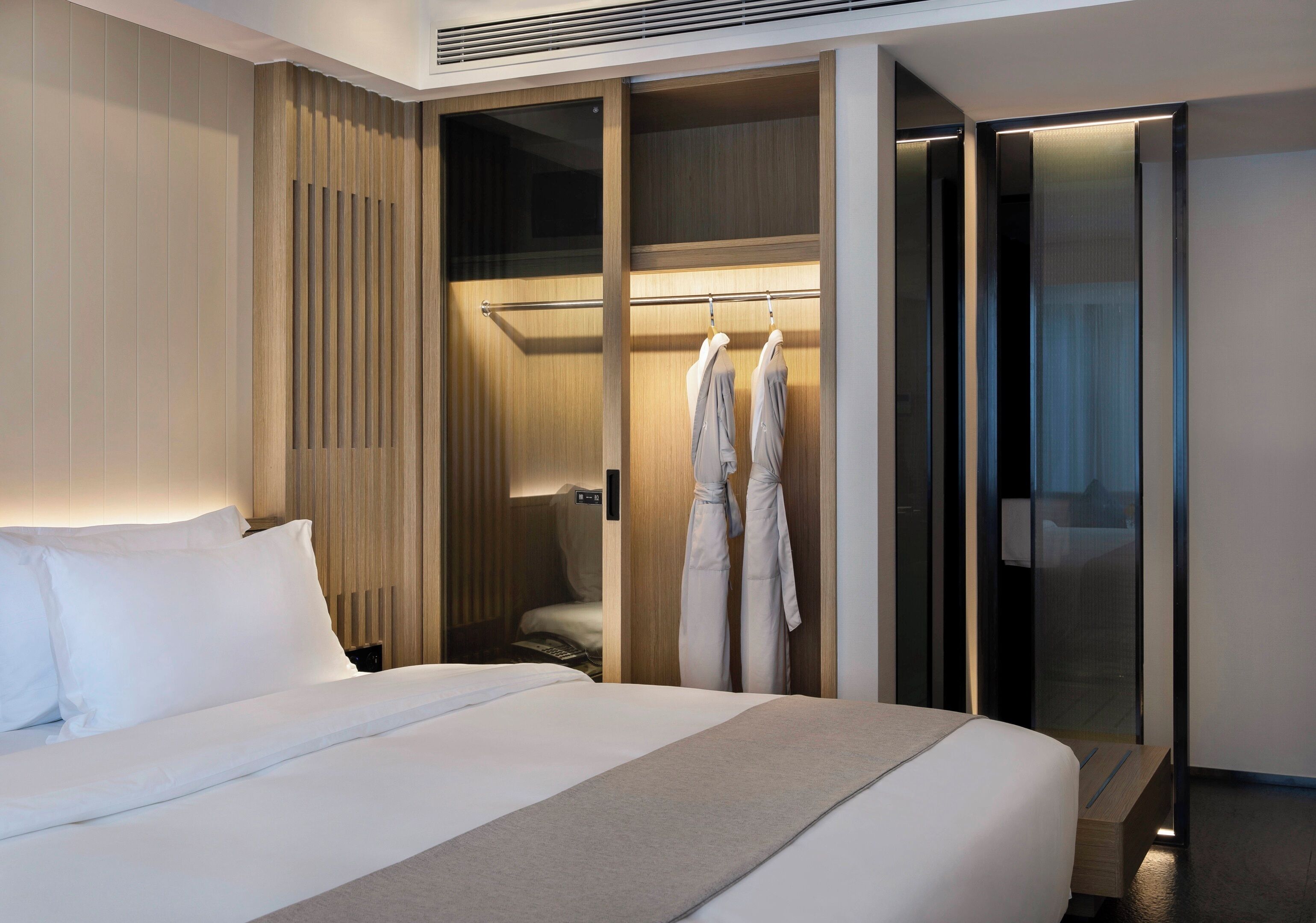 A hotel room with a large bed, a wardrobe with a mirror, and a robe rack with two robes.