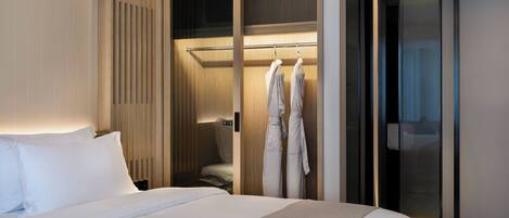 A hotel room with a large bed, a wardrobe with a mirror, and a robe rack with two robes.