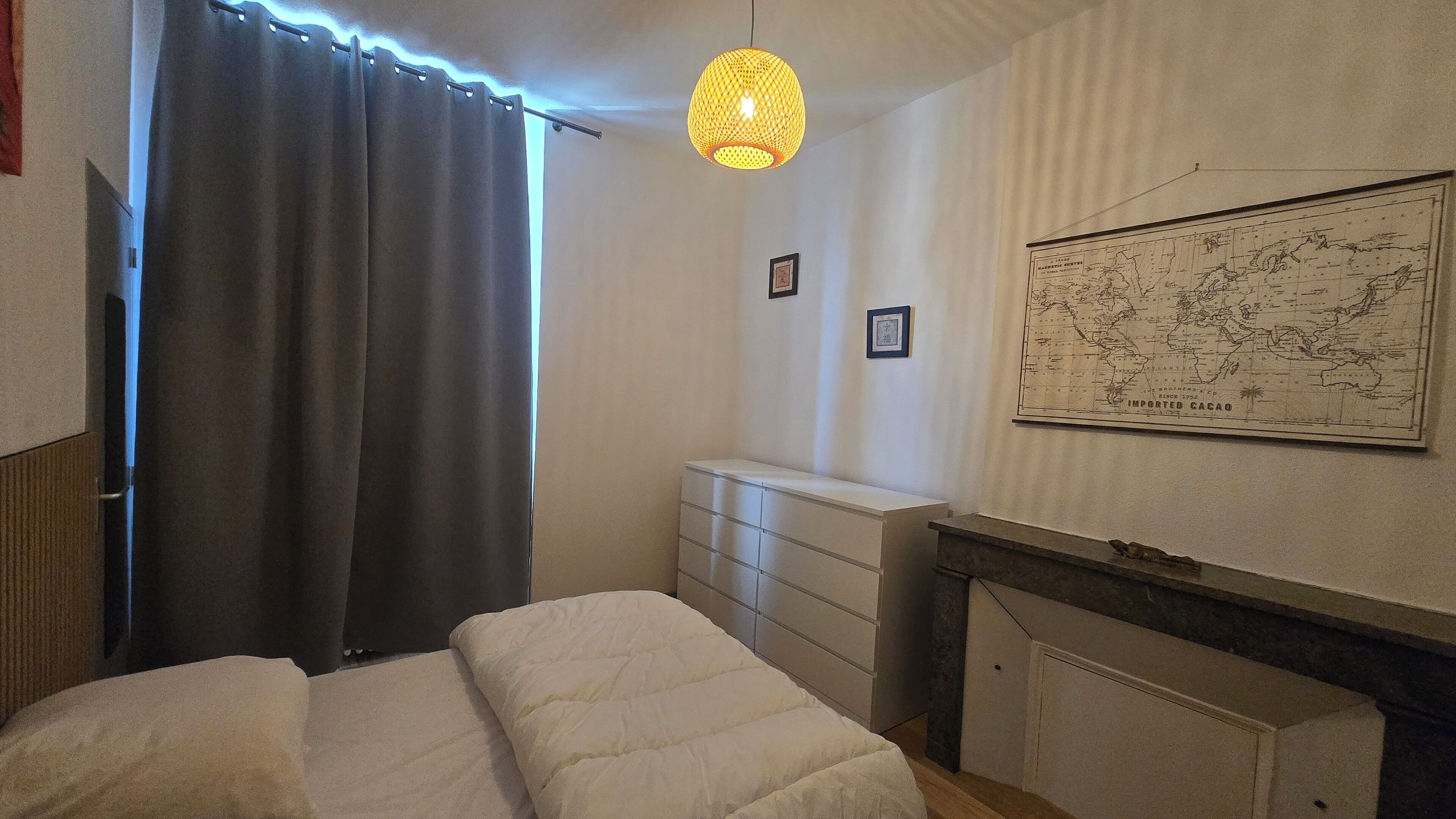 A bedroom with a bed, a dresser, a map on the wall, and a hanging light fixture.