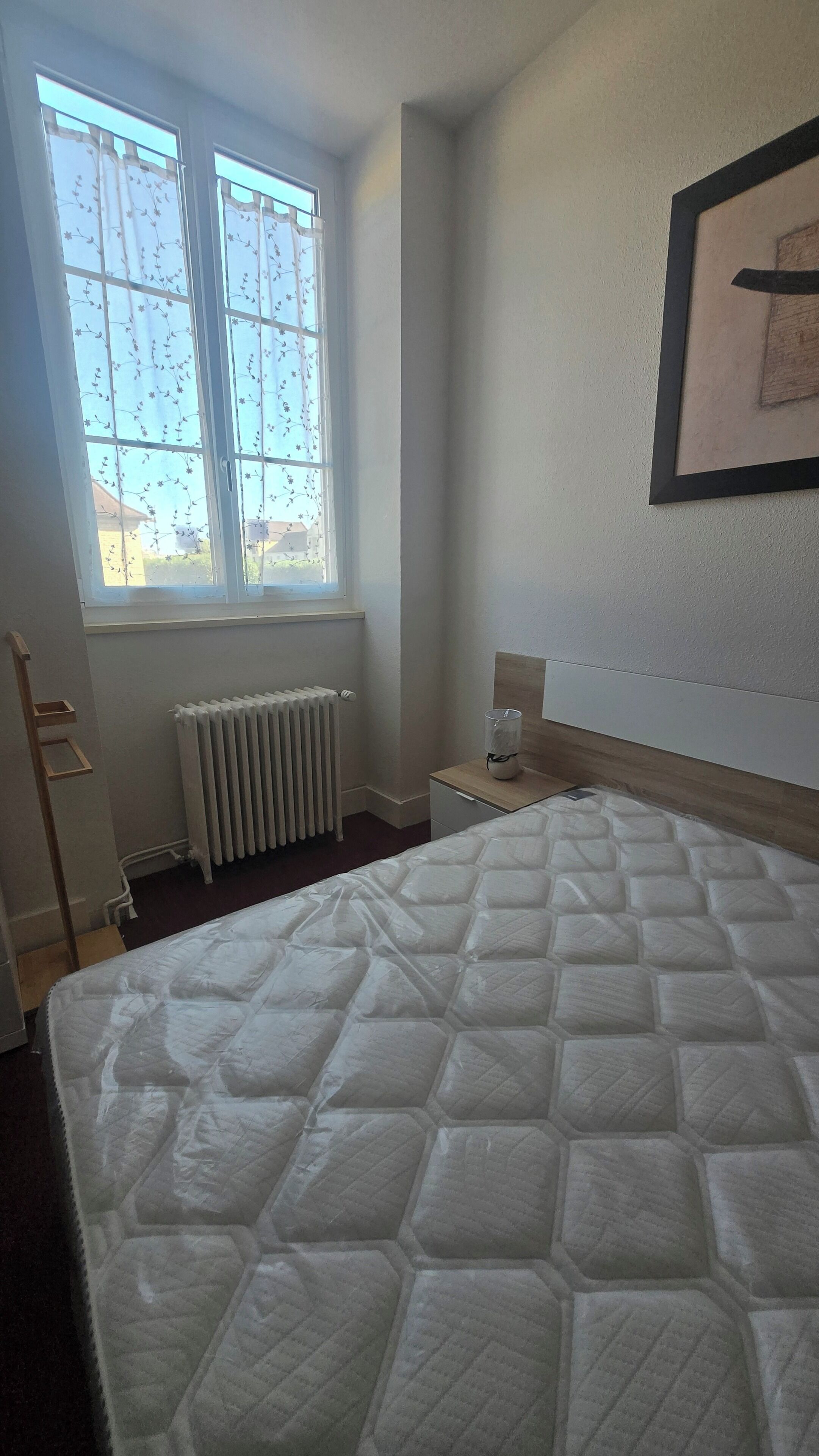 Un dormitorio con una cama grande, un radiador, una ventana con cortinas y un cuadro en la pared.