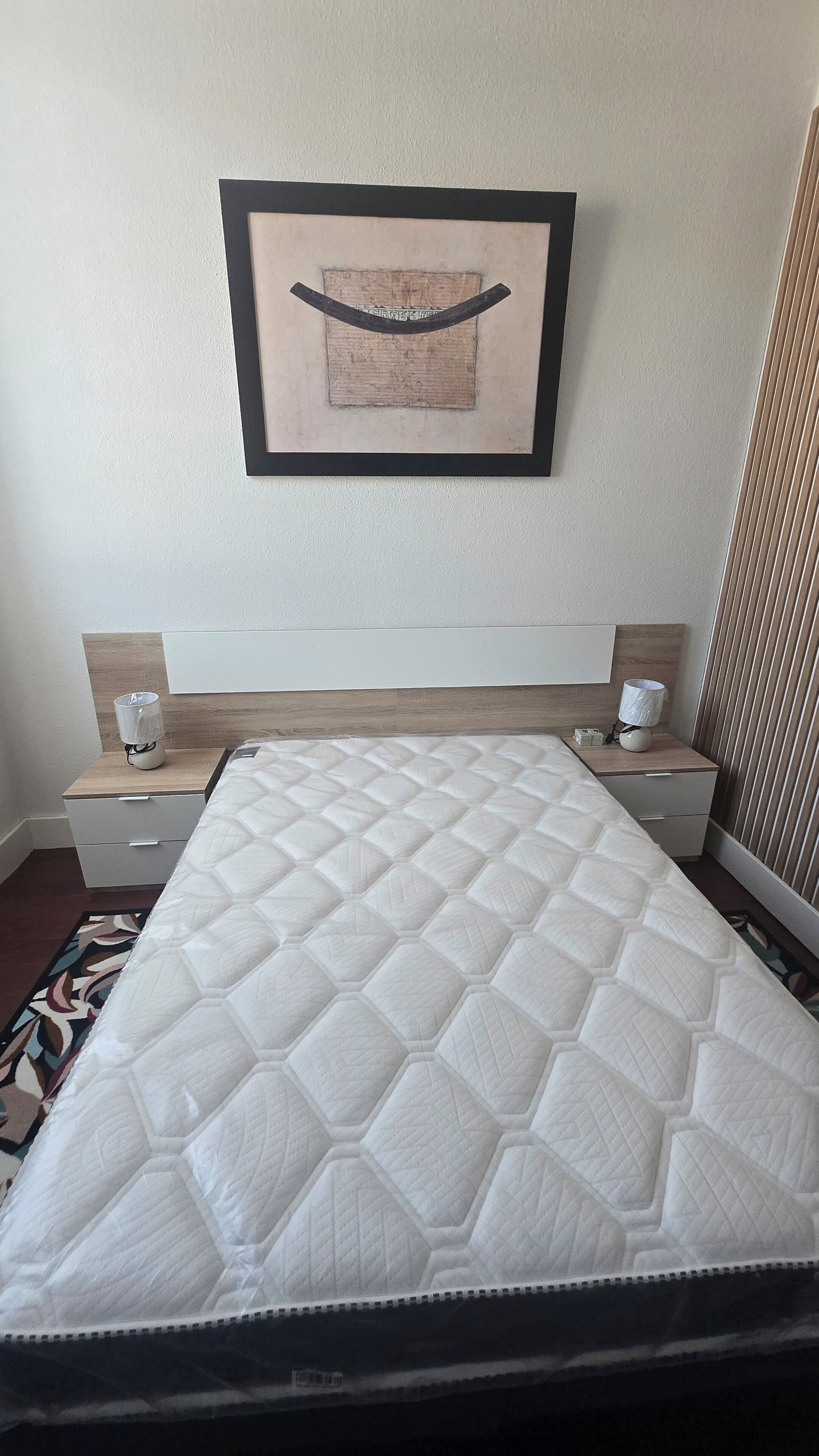 A hotel room with a large bed, two bedside tables, a headboard, and a framed artwork on the wall.