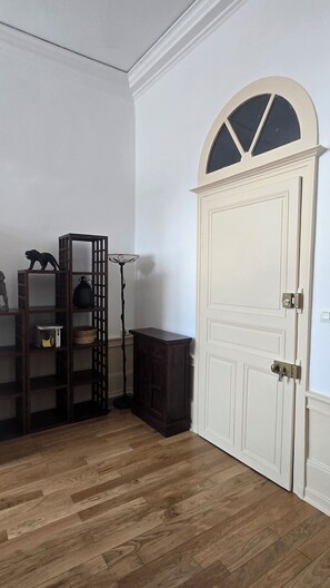 A room with a wooden floor, a white door with a decorative arch, and a wooden shelving unit with various items.