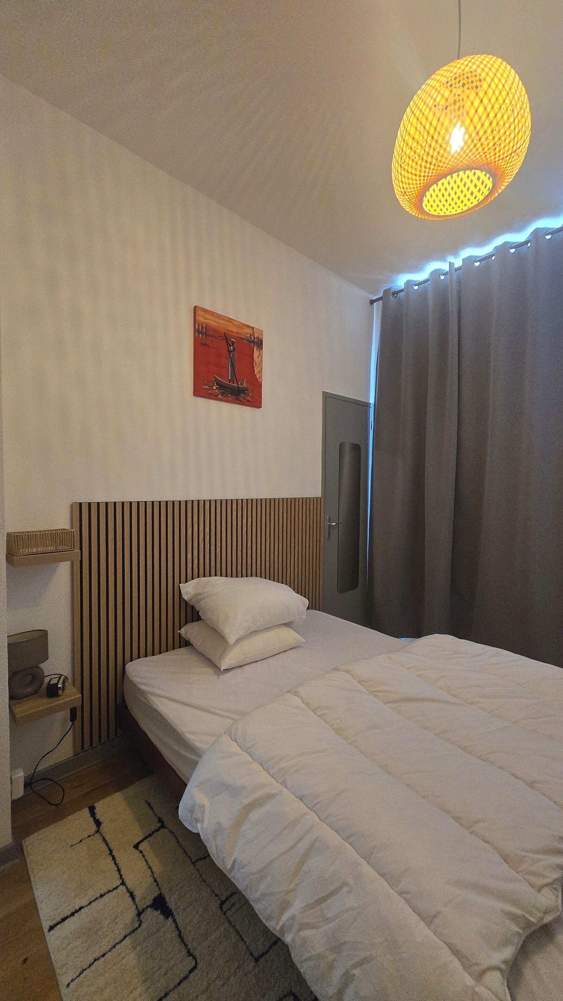 Habitación de hotel con cama, mesita de noche con lámpara, cuadro colgado en la pared, armario y lámpara colgante.