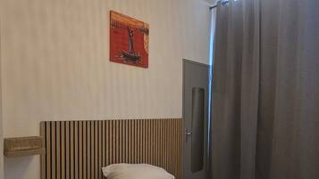 Habitación de hotel con cama, mesita de noche con lámpara, cuadro colgado en la pared, armario y lámpara colgante.