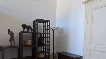 Una habitación de esquina con piso de madera, un mueble de madera oscura, una puerta blanca con arco decorativo y un estante con adornos.