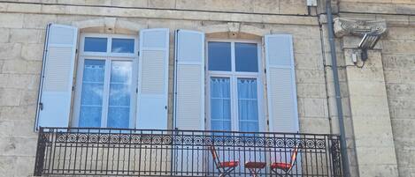 A building facade with a balcony featuring a wrought iron railing and two red chairs.