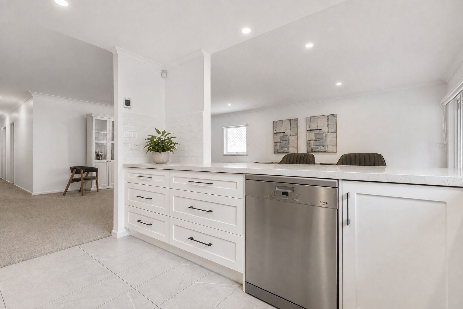 A modern kitchen with white cabinetry, a dishwasher, and a potted plant.