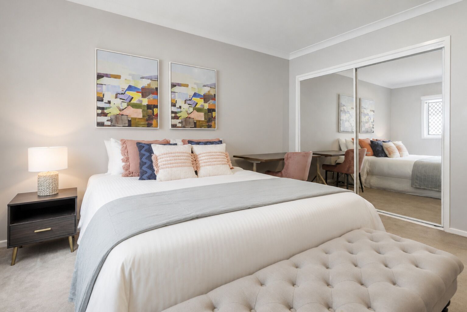 A bedroom with a large bed, a desk, and a chair. There are two wall-mounted artworks above the bed.