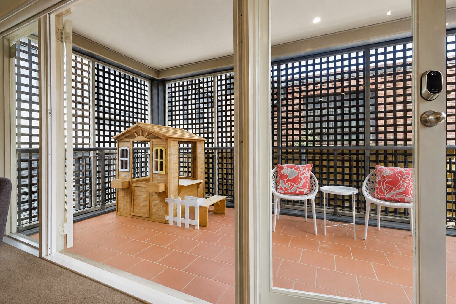 A balcony with a wooden playhouse, two white chairs with red cushions, and a metal gate.