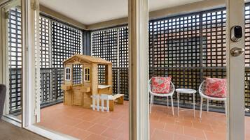 A balcony with a wooden playhouse, two white chairs with red cushions, and a metal gate.